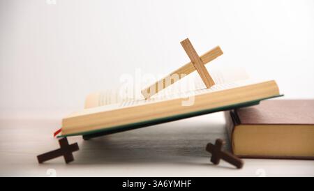 Open Bible on a wooden table with several wooden crosses and isolated white background. Side view. Stock Photo