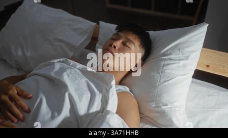 Young man sleeping in a comfortable bed at home, capturing a peaceful indoor moment in a cozy bedroom setting. Stock Photo