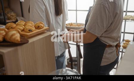 Women working together in a bakery shop as bakers adjusting aprons near freshly baked pastries in an indoor room Stock Photo