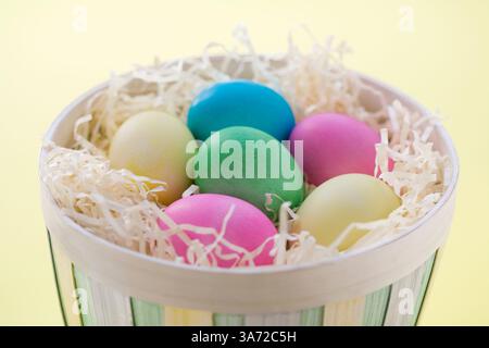 Pastel-colored Easter eggs in basket against yellow background Stock Photo