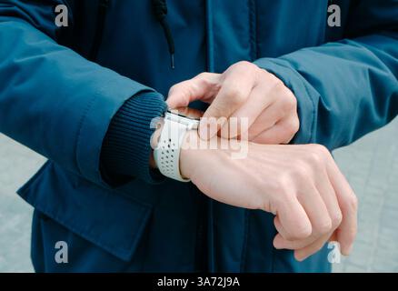 a man, wearing a navy blue coat, activates the GPS tracker of his smartwatch on the street, on a winter day Stock Photo