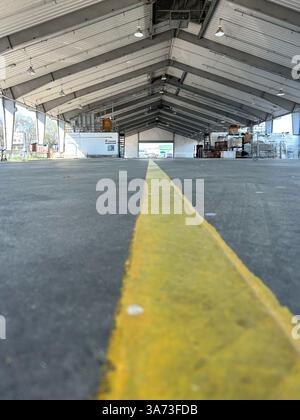 A yellow line is painted on a grey concrete floor. The line is in the middle of the floor and is surrounded by a white line. The floor is empty and th Stock Photo
