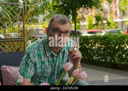 A man relaxes on a patio chair, surrounded by lush green plants and vibrant pink tulips. Stock Photo