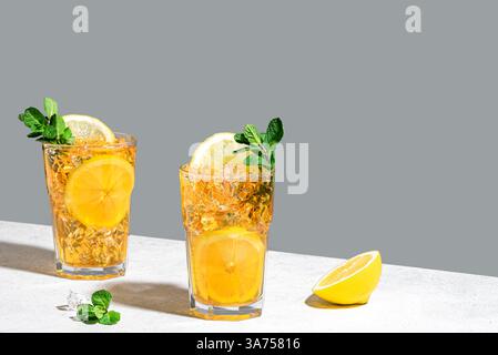 Ice tea with lemon. Two glasses of iced tea with lemon slices, mint and ice cubes on white and gray background, trendy hard light with shadows,  copy Stock Photo