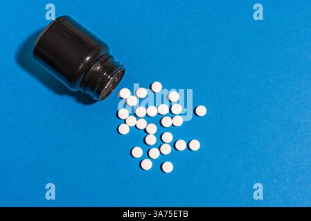 Melatonin tablets spill from black container on dark blue background, top view. Jar of dietary supplement for healthy sleeping. Insomnia and biohackin Stock Photo
