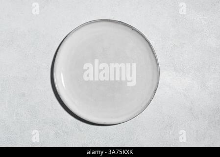 Empty gray plate on gray concrete table, top view, copy space. Design template with light grey ceramic plate. Stock Photo