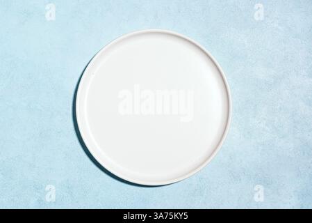 Empty white plate on blue concrete table, top view, copy space. Design template with white ceramic plate. Stock Photo