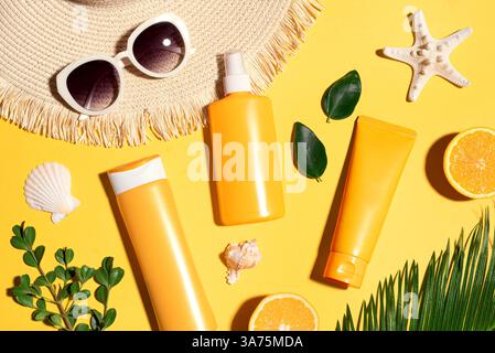 Summer vacation, UV protection concept. Orange sunblock products, sunglasses, straw hat, starfish and palm leaves on yellow background. SPF sunscreen Stock Photo