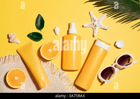 Summer vacation, UV Ultraviolet protection concept. Orange sunblock products, sunglasses, straw hat, starfish and palm leaf on bright yellow backgroun Stock Photo