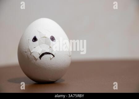 Cracked chicken egg with sad and sorrowful emotions on table drawn on egg, egg shortage in 2025 Stock Photo