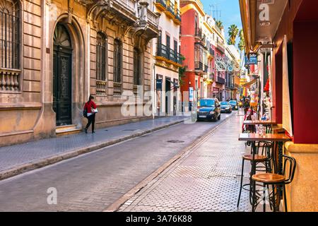 A narrow street of traditional of sidewalk cafes and shops in downtown district of the Andalusian city of Seville, Spain. Stock Photo