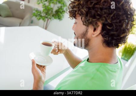 Young man enjoying a cup of tea indoors, showcasing comfort and leisure during a peaceful moment in a bright and welcoming home Stock Photo
