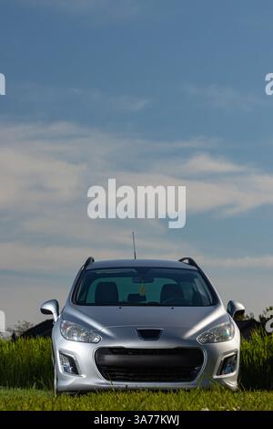 A modern silver car is parked in a field under a clear blue sky, showcasing its stylish design and headlight symmetry. Stock Photo