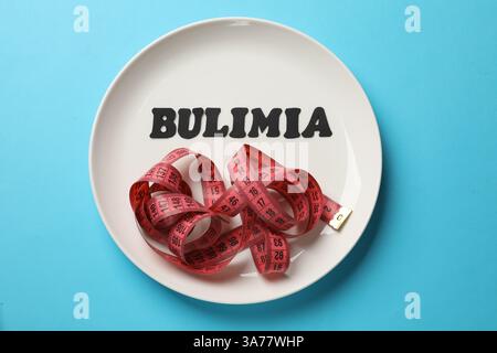 Plate with word Bulimia and measuring tape on light blue background, top view Stock Photo