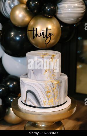 A beautifully crafted two-tier cake features marbled patterns and gold highlights for a milestone birthday celebration. Stock Photo