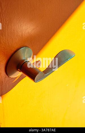 A metal door handle in brass colour on a wooden door and yellow background. Stock Photo