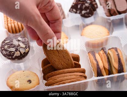 Woman hand taking cookie from the plastic box with different kinds of cookies in it. Stock Photo
