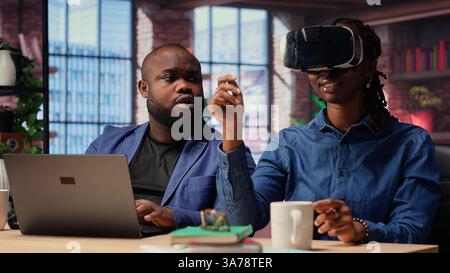 Black people integrate VR and AI into their daily job routine where the man engages in immersive 3D experience. Young focused woman reviews the animation on headset within the metaverse. Camera B. Stock Photo