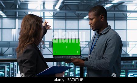 Engineering team in data center using green screen laptop, implementing predictive analytics scripts, reviewing equipment health, adjusting system parameters, coordinating maintenance tasks, camera A Stock Photo