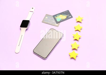 Five stars with mobile phone, smartwatch and credit cards on lilac background. Customer experience concept Stock Photo