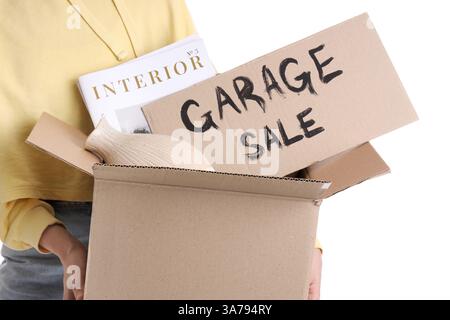Woman holding box of unwanted stuff and cardboard with text GARAGE SALE on white background Stock Photo
