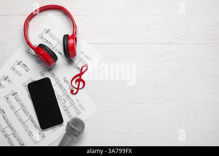 Modern mobile phone, music sheets, headphones and microphone on white wooden background Stock Photo
