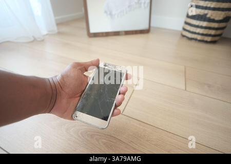 Broken smartphone in hand on wooden floor indoors Stock Photo
