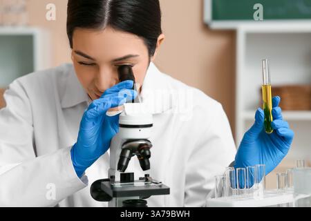 Female inventor with test tube looking through microscope in laboratory, closeup Stock Photo