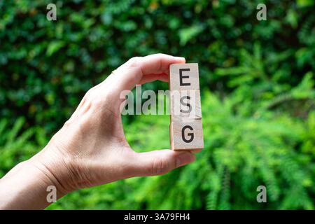 Hand holding three wooden blocks with word ESG. Green nature background. Stock Photo