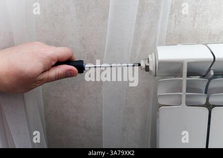 adjusting pressure from the radiator using a screwdriver. Home heating battery repair Stock Photo