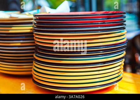 Stack of colorful plates, including red, yellow, green, and blue, is neatly arranged on a table. Another stack is partially visible, suggesting a live Stock Photo