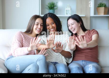 Three happy friends comparing manicure sitting on a couch at home Stock Photo