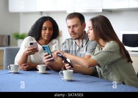Three roommates checking their phones in the kitchen at home Stock Photo