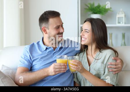 Happy couple toasting with orange juice glasses looking each other at home Stock Photo