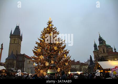 Festive Christmas tree with golden star decorations and lights in Prague's Old Town Square, surrounded by crowds and historic architecture. Stock Photo
