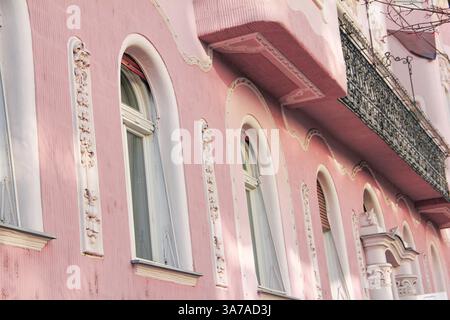 Detailed view of an Art Nouveau building facade in pink with ornate white stucco decorations and a black wrought iron balcony in a city setting. Stock Photo