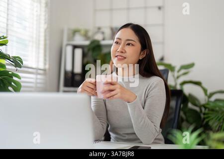 Work and Productivity. A young woman enjoys a warm beverage while contemplating her tasks at home. Stock Photo