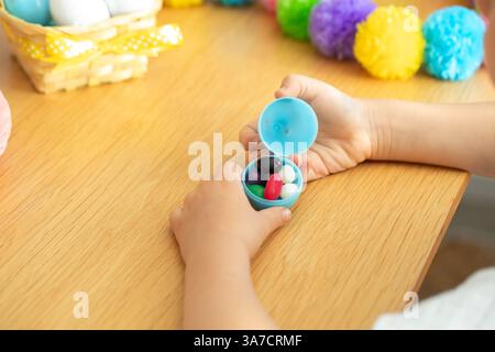Child opening easter egg with colorful candy surrounded by festive decorations for spring celebration. Easter.  Stock Photo