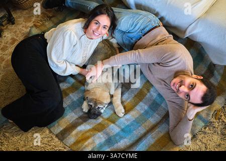 Young smiling couple is lying on a blanket at home and petting their puppy Stock Photo