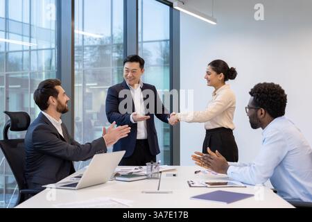 A diverse group of colleagues celebrates a new partnership with a handshake in a modern office, showing team support and success. Stock Photo