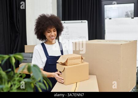 A young woman smiles while organizing boxes and packages in a modern office setting. Stock Photo