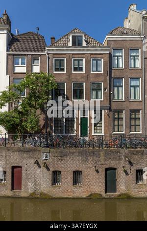 Front view of the Oudegracht canal with wall and doors for the entrance to the basement. A steel fence with bicycles and brick houses on a sunny day a Stock Photo