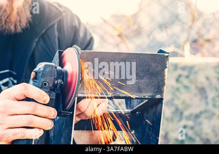 Hand using angle grinder to cut metal with sparks in outdoor construction site Stock Photo