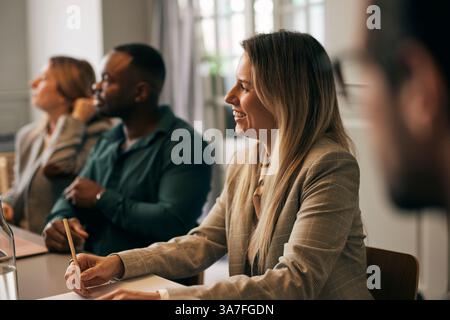 Happy female creative business professional taking notes during meeting with colleagues in office Stock Photo