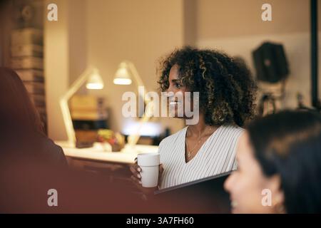 Happy curly haired young businesswoman holding disposable cup at office Stock Photo