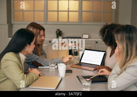 Female creative business professionals discussing plan over laptop while sitting in meeting room at office Stock Photo