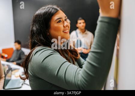 Smiling young woman writing on whiteboard in classroom at college Stock Photo