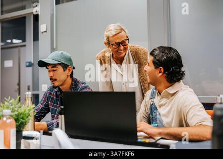 Smiling female professor talking with male student studying on laptop in university classroom Stock Photo