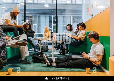 Young man listening to music while using smart phone and sitting near friends studying in college Stock Photo