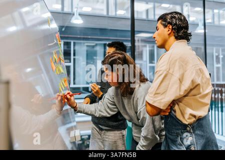 Young woman writing on whiteboard while standing with male classmates in tech university Stock Photo